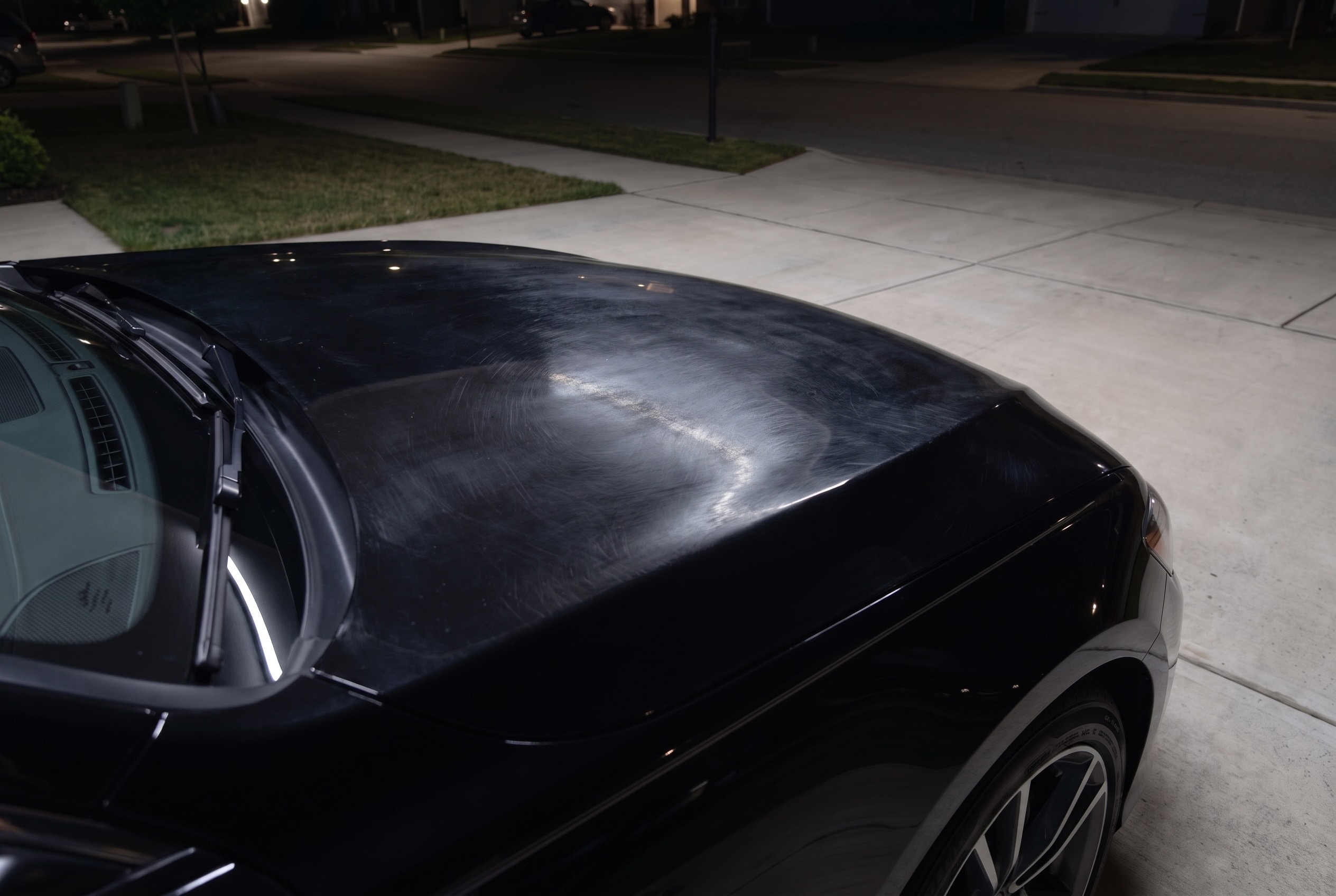 Black car hood covered in swirl marks and wash haze before paint correction
