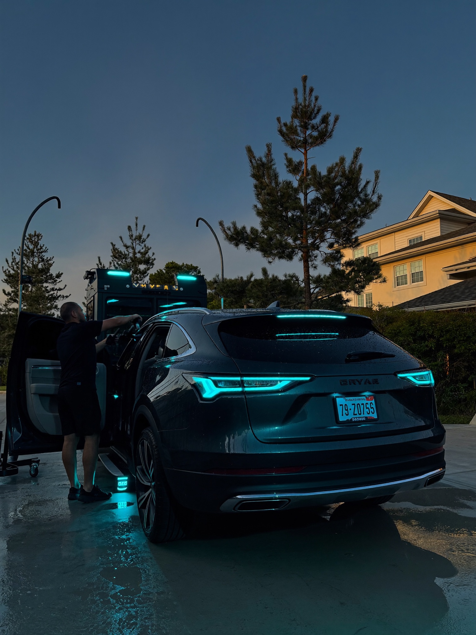 Detailer working on a premium dark SUV in a Fayetteville NC driveway at dusk with the mobile detailing rig alongside